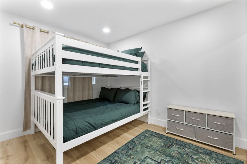 Bedroom with a queen-over-queen bunk bed in green bedding and a dresser
