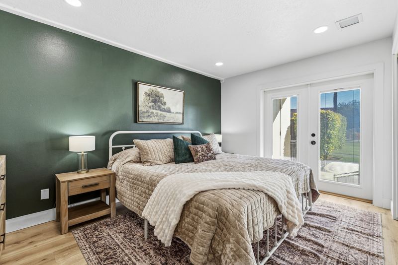 King bedroom with a green accent wall, nightstands, and French doors to the patio