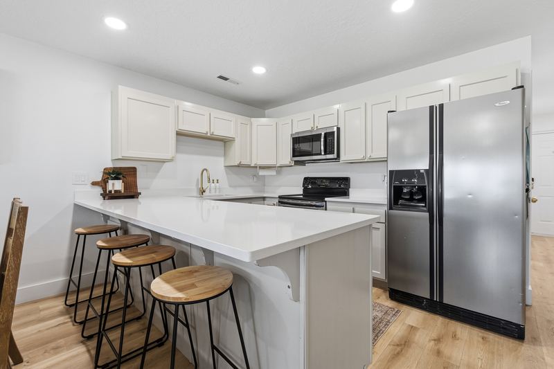 Kitchen with a breakfast bar and four stools, stainless refrigerator, and brass faucet