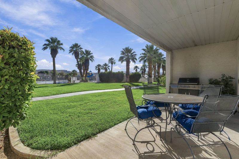 Patio with seating and a BBQ grill looking out on the lawn and palm trees