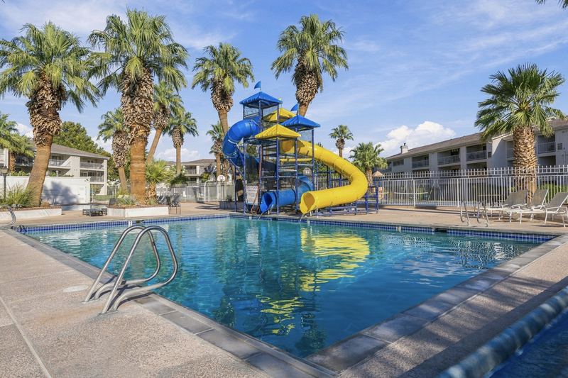 Outdoor pool with a blue and yellow waterslide tower under palm trees